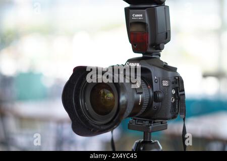 Black Canon DSLR camera mounted on a tripod with an external flash ready to use Stock Photo