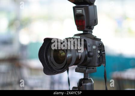 Black Canon DSLR camera mounted on a tripod with an external flash ready to use Stock Photo
