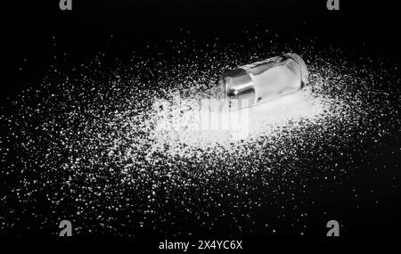 Scattered salt on a black background and a stem salt shaker. Close-up Stock Photo