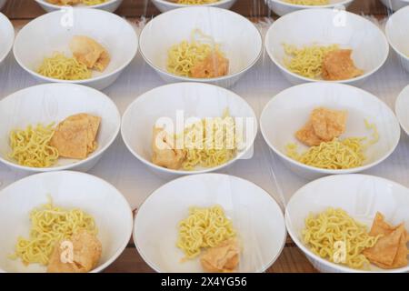 Several white bowls containing yellow noodles, fried foods and meatballs without sauce on the table Stock Photo