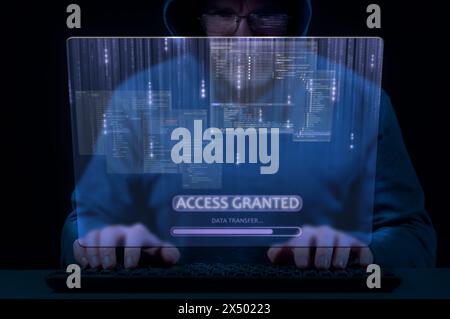 Man in hood on dark background uses keyboard and virtual screen to break cybersecurity system Stock Photo
