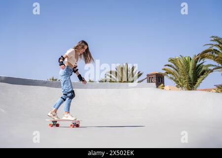 A beginner young woman is actively surfing on a skateboard down the side of a ramp. Stock Photo