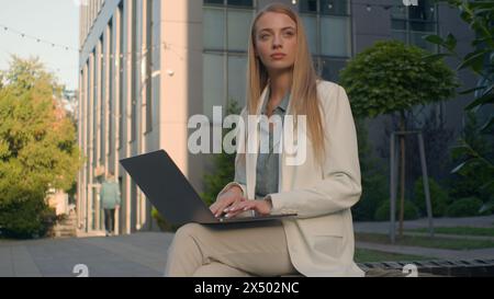 Pensive Caucasian woman businesswoman student female business lady girl developer think typing on laptop outdoors street near office work remote Stock Photo