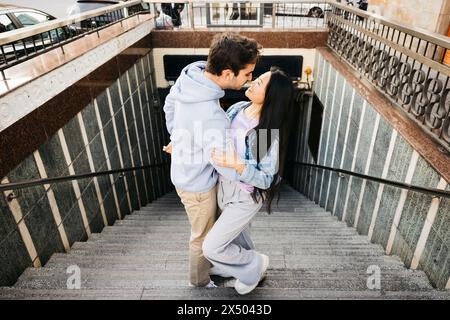 Interracial cheerful couple on a date, getting off the subway in a city. Young man and woman kissing on subway stairs. Stock Photo
