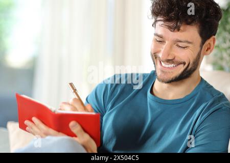 Happy man writing in agenda sitting on a couch at home Stock Photo