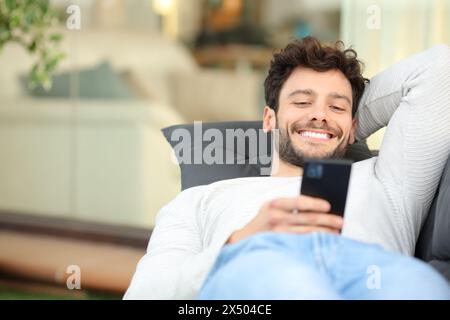 Happy man lying on a couch in a home terrace using phone Stock Photo