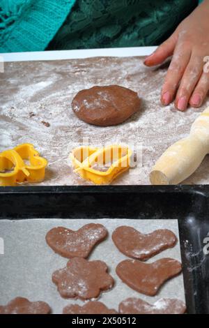 Before the woman a lump of dough for rolling. The working surface is in flour, the tools lie next to it. On the baking tray baking dish. Cooking ginge Stock Photo