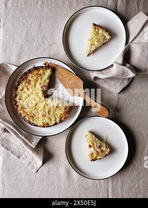 Overhead view of a homemade cheese and onion quiche and two slices on plates for lunch Stock Photo