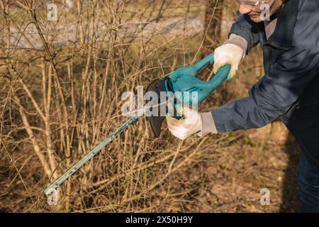 A man working in the garden, trimming branches with an electric hedge trimmer. Stock Photo