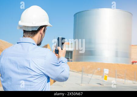Engineer in hard hat takes pic of tank using cell phone Stock Photo