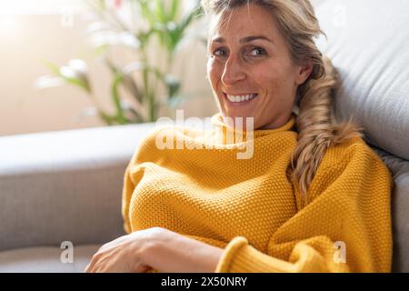 Mature woman in yellow sweater relaxing on sofa with a bright smile Stock Photo
