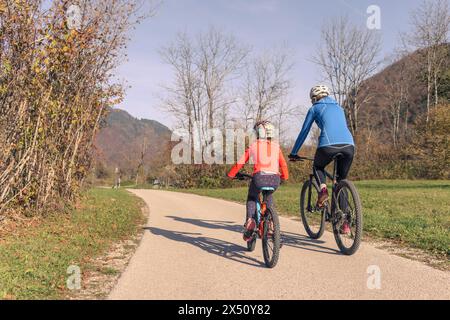 Two cyclists, a mother with a girl child on a bike ride along the road in rural nature. Family recreation concept. Stock Photo