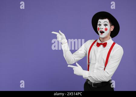 Funny mime artist pointing at something on purple background. Space for text Stock Photo