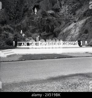 1960s, historical, religious grotto, a concrete balustrade stating.. 'I am the Immaculate Conception'....Ballinspittle, Ireland, behind a ravine with a plaster statue of a woman, the virgin mary. A gentleman on right of picture kneeling down in prayer. In 1985 a local woman and the caretaker of the grotto is said to have seen the statue move and become life-like. Stock Photo