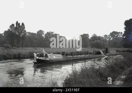 1950s, historical, lady steering a long working narrowboat, G. U. C. C. Co. Ltd 275 along a canal, England, UK. Registered at Ealing on the side of the boat. A man on another GUCC boat in front, both being boats of The Grand Union Canal Carrying Co Ltd, a freight carrying canal transport serivce which operated between 1934 to 1948. Stock Photo