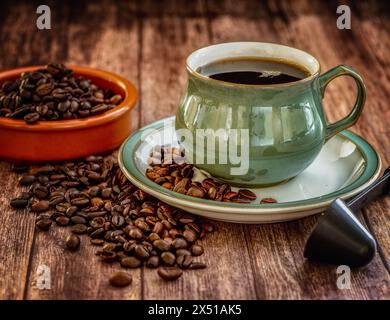 Green Coffee cup and saucer close-up over dark roasted coffee beans on wooden table. Stock Photo