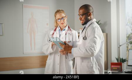Doctor's Office: Black Physician Talks With Professional Head Nurse, Using Tablet Computer. Medical Health Care Specialists Discussing Test Results, Prescription Medicine, Patient Treatment. Stock Photo