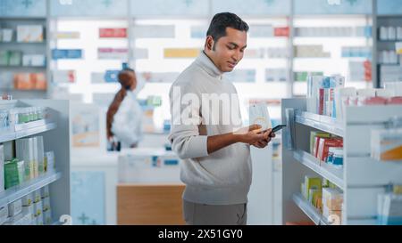 Pharmacy Drugstore: Portrait of a Handsome Young Indian Man Using Smartphone Device, Chooses to Purchase Best Medicine, Drugs, Vitamins. Shelves full of Sport Supplements, Health Care Products Stock Photo