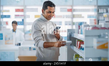 Pharmacy Drugstore: Portrait of a Handsome Young Indian Man Using Smartphone Device, Chooses to Purchase Best Medicine, Drugs, Vitamins. Shelves full of Sport Supplements, Health Care Products Stock Photo