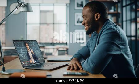 African American Man Having an Online Video Lesson on Laptop Computer while Sitting Behind Desk in Living Room. Freelancer Working on His Skills or Student Doing Homework Over the Internet. Stock Photo