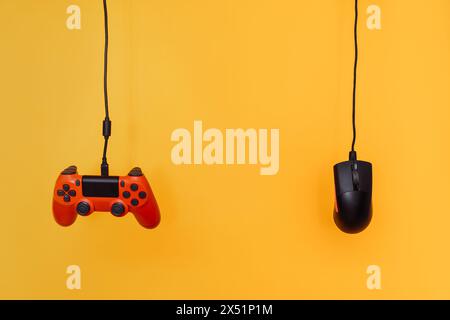 A red gamepad and a computer mouse hang on wires against a yellow background Stock Photo