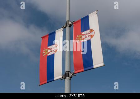 Pair of Serbian flags outdoors on a pole with a cloudy sky behind. Stock Photo