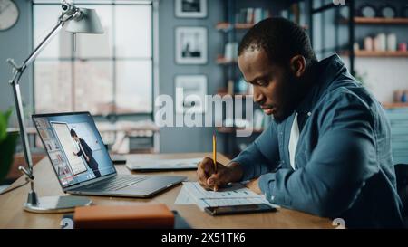 African American Man Having an Online Video Lesson on Laptop Computer while Sitting Behind Desk in Living Room. Freelancer Working on His Skills or Student Doing Homework Over the Internet. Stock Photo