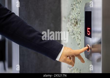 A professional businessman in a dark suit pressing an elevator button, symbolizing convenience and modern corporate life in an urban setting. Stock Photo