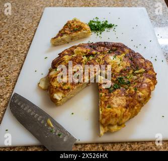 A sliced Spanish tortilla garnished with parsley on a cutting board, with a knife next to it. This traditional Spanish potato omelet dish Stock Photo