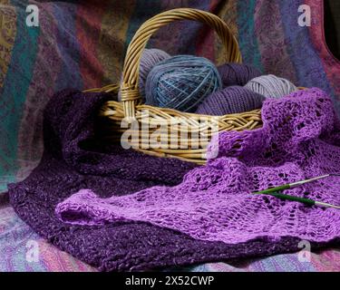 Purple knitted shawl with basket of yarn in background Stock Photo