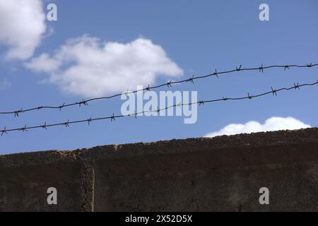 A concrete wall with barbed wire on top against a blue sky background Stock Photo