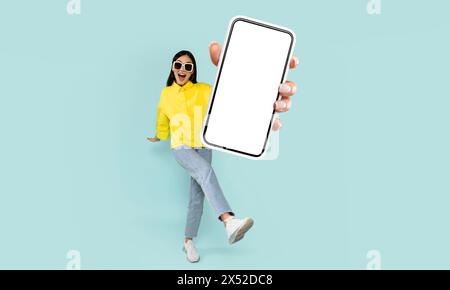 Woman in Yellow Shirt Presenting Smartphone With Blank Screen Stock Photo