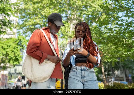 Focused black girl uses city map app on smartphone with interested man trying to get right direction Stock Photo