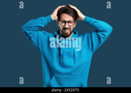 Man in Blue Hoodie Expressing Frustration With Hands on Head Stock Photo