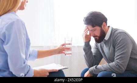 Psychoanalyst offering glass of water to depressed male patient Stock Photo