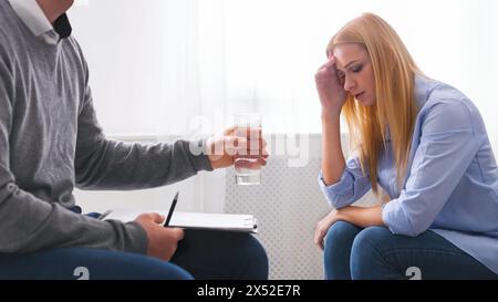 Psychotherapist offering glass of water to upset crying female patient Stock Photo