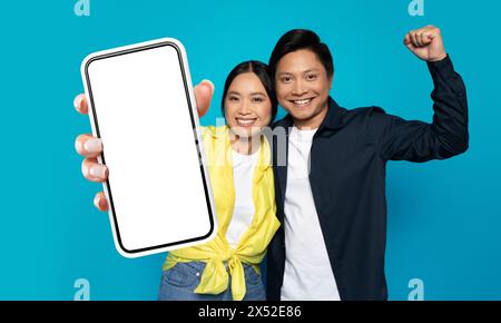 Cheerful Young Asian Couple Holding Up a Cell Phone Stock Photo
