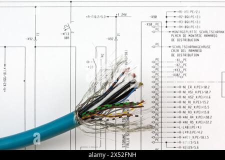 In front of the electrical circuit diagram lies a stripped multiconductor cable with visible, color-coded wires ready to establish new connections. Stock Photo