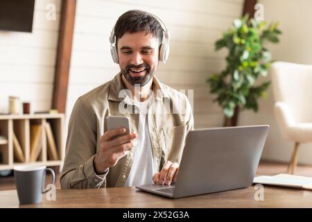 Smiling Man With Headphones Using Smartphone and Laptop Stock Photo