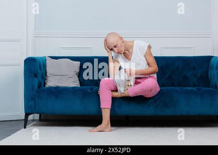 Bald woman sits distressed on couch tired of chemo treatment Stock Photo