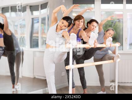 Woman with group of ballet beginners stretching at barre in studio Stock Photo