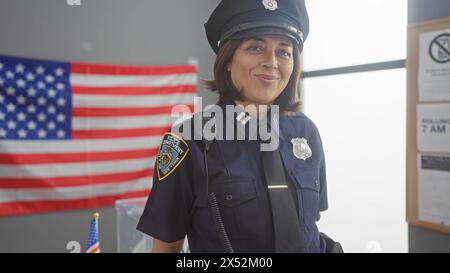 A smiling hispanic policewoman in uniform stands before an american flag in a well-lit room. Stock Photo