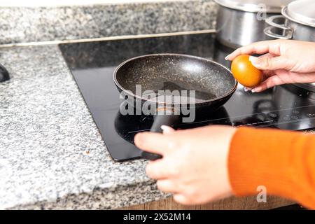 close-up of hands that are going to break an egg to fry it in a frying pan on an induction cooker with oil Stock Photo