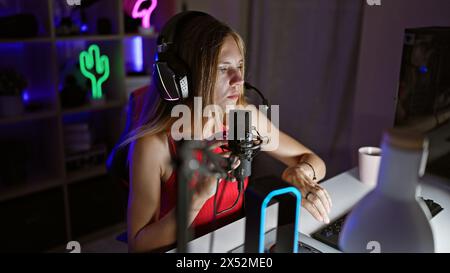 A focused woman in a gaming room with neon lights using a microphone and wearing headphones at night. Stock Photo