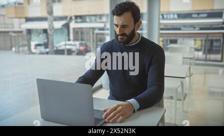 Middle-aged bearded man working intently on laptop in modern office environment Stock Photo