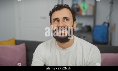 Close-up of a smiling bearded man lounging comfortably in a modern living room, exhibiting casual relaxation. Stock Photo