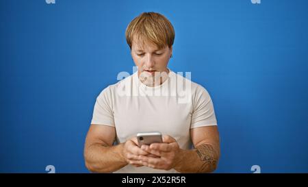 Handsome young caucasian man with a beard and tattoos using a smartphone against a blue wall background outdoors Stock Photo