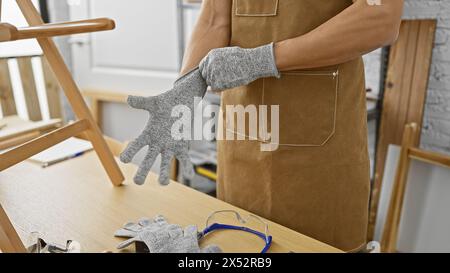 A hispanic man prepares to work by putting on gloves in a well-equipped carpentry workshop. Stock Photo