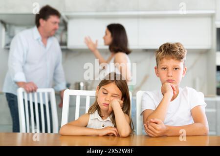 Brother and sister sit at table during quarrel between parents Stock Photo