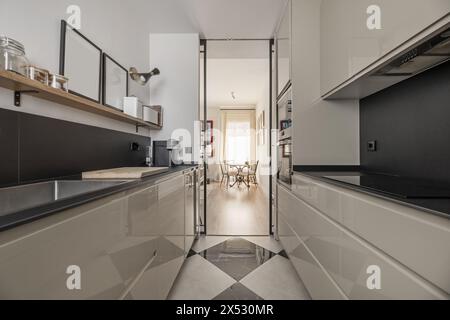 Modern kitchen furnished with black countertops and backsplashes and checkered floors Stock Photo